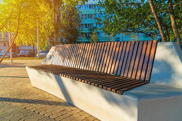 A modern concrete bench covered with brown wooden slats in a city park. - obrazy, fototapety, plakaty