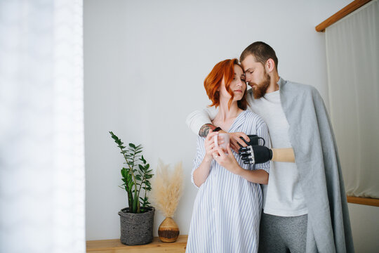 Weary Thirty Year Old Couple Touching Foreheads, Holding Coffee Mugs