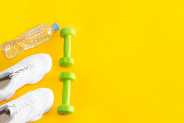 Fitness accessories for women. White athletic shoes, dumbbells, a drinking bottle. An empty space for a motivating, inspiring text. The concept of a healthy lifestyle.