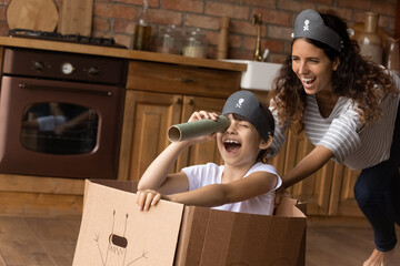 Excited kid and happy laughing mom playing pirates at home, sailing toy paper ship, looking forward...