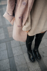 stylish image of urban fashion. knitted beige dress, pink delicate raincoat, black high boots on woman without face. autumn female look. cozy stily clothes. selective focus