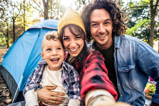 Happy family camping in the forest taking selfie portrait together - Mother, father and son having fun trekking in the nature sitting in front of the tent - Family, nature and trekking concept