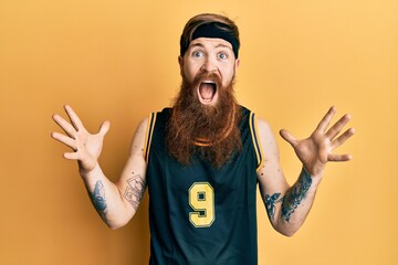 Redhead man with long beard wearing basketball uniform celebrating crazy and amazed for success with arms raised and open eyes screaming excited. winner concept