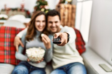 Young hispanic couple watching movie and eating popcorn sitting on the sofa at home.