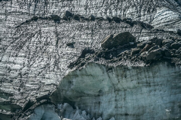 Fototapeta premium Nature background with icefall near glacier with cracks and scratches. Natural backdrop with icy wall and moraines. Beautiful landscape with shiny glacial wall and stones in sunlight. Glacier texture.