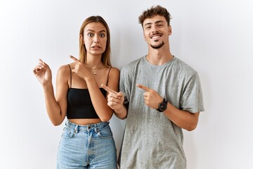 Young beautiful couple standing together over isolated background pointing aside worried and nervous with both hands, concerned and surprised expression