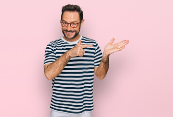 Fototapeta premium Middle age man wearing casual clothes and glasses amazed and smiling to the camera while presenting with hand and pointing with finger.