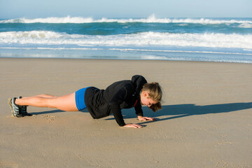 pretty young woman doing push-ups on the sunny beach