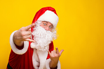 Fototapeta na wymiar Snata claus makes horns with his fingers. Rock santa on yellow isolated background
