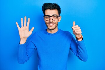 Fototapeta premium Young hispanic man wearing casual clothes and glasses showing and pointing up with fingers number six while smiling confident and happy.