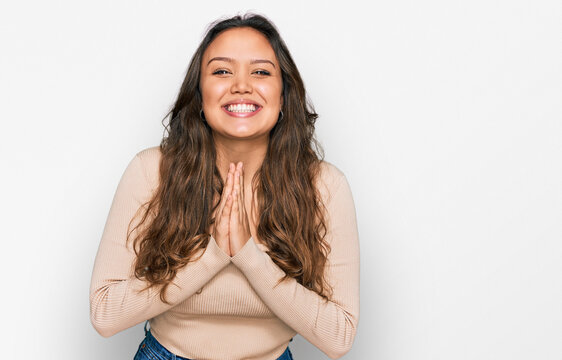 Young hispanic girl wearing casual clothes praying with hands together asking for forgiveness smiling confident.