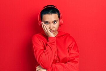 Beautiful hispanic woman with short hair listening to music using headphones thinking looking tired and bored with depression problems with crossed arms.