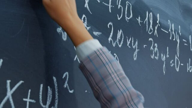 Female hand with chalk. Math faceless teacher writes examples for schoolchildren on blackboard. Student, pupil girl solves system of equations on chalkboard. Algebra, mathematics in classroom