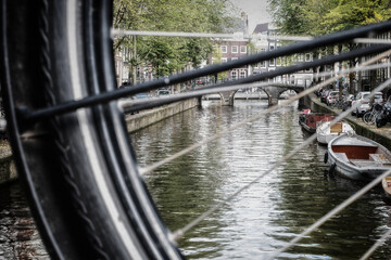 Blick durch die Speichen eines Fahrrads in eine Gracht (Amsterdam, Niederlande)