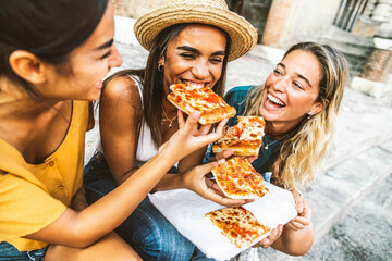 Three young female friends sitting outdoor and eating pizza - Happy women having fun enjoying a day out on city street - Happy lifestyle and tourism concept