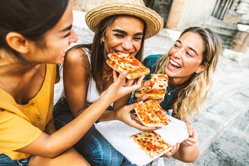 Three young female friends sitting outdoor and eating pizza - Happy women having fun enjoying a day out on city street - Happy lifestyle and tourism concept - Powered by Adobe