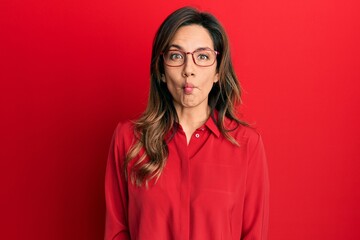 Young latin woman wearing casual clothes and glasses making fish face with lips, crazy and comical gesture. funny expression.