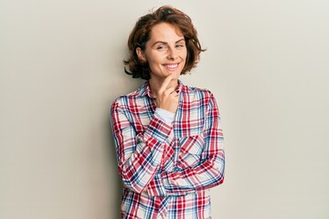 Young brunette woman wearing casual clothes smiling looking confident at the camera with crossed arms and hand on chin. thinking positive.