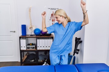 Young physiotherapist woman working at pain recovery clinic dancing happy and cheerful, smiling moving casual and confident listening to music