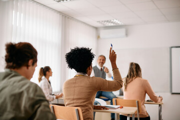 Rear view of female black student with raised arm during lecture in classroom.