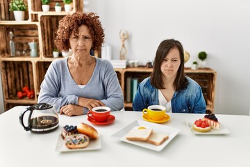 Family of mother and down syndrome daughter sitting at home eating breakfast skeptic and nervous, frowning upset because of problem. negative person.
