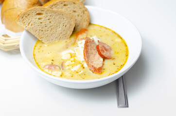 Traditional polish sour soup with sausage and eggs in ceramic bowl