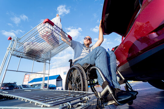 Person with a physical disability puts purchases in the trunk of a car in a supermarket parking lot