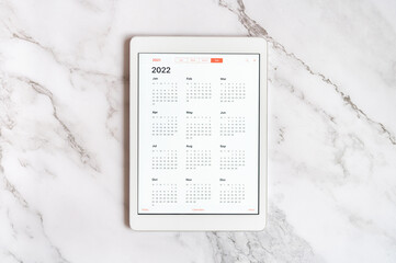 tablet computer with an open app of calendar for 2022 year on a gray marble background. concept...