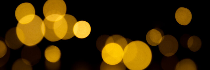 Bokeh golden lights background. Blurred lights festive garland on a black background. Banner size