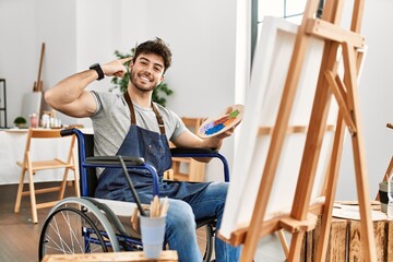 Young hispanic man sitting on wheelchair painting at art studio smiling pointing to head with one finger, great idea or thought, good memory