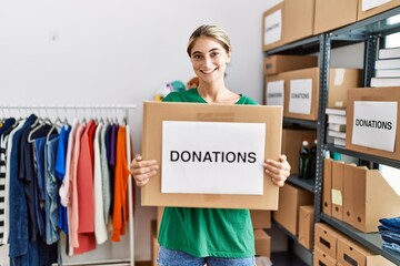 Young caucasian woman wearing volunteer uniform holding donations box at charity center