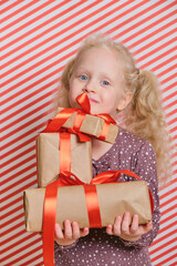 cute cheerful preschooler girl with gifts on a red striped background, gifts with a red ribbon