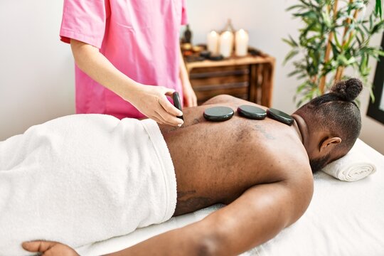 Young african american man having back massage with hot stones at beauty center