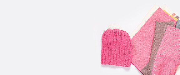 Pink hat and striped scarf on a white background. Top view, flat lay. Banner.