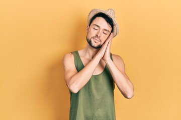 Young hispanic man wearing summer hat sleeping tired dreaming and posing with hands together while smiling with closed eyes.