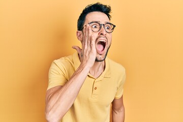 Young hispanic man wearing casual clothes and glasses shouting and screaming loud to side with hand on mouth. communication concept.