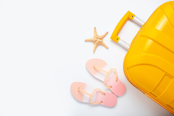 Yellow suitcase, beach flip flops, starfishes on a white background. Top view, flat lay.