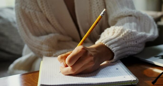 A woman makes notes in notebook with her left hand, sitting near open laptop