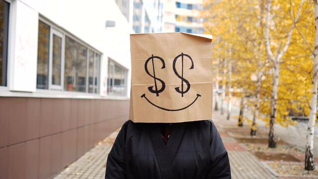 Rich paper bag face walking along street. Funny woman in bag of bread on which dollars are drawn