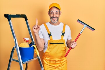 Handsome middle age man with grey hair wearing glass cleaner uniform and squeegee smiling with an idea or question pointing finger with happy face, number one