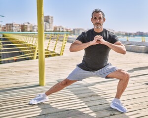 Middle age hispanic man wearing sportswear stretching at seaside