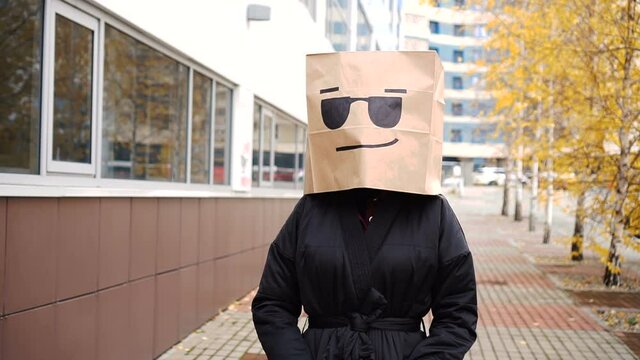 Cool bright paper bag face walking along street. Confident woman wearing bread bag with sunglasses