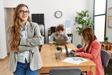 Manager smiling happy standing with arms crossed gesture. Business employees working at the office.