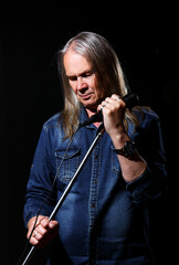 elderly man with long gray hair sings into a microphone