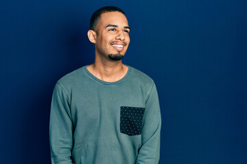 Fototapeta premium Young african american man wearing casual clothes looking away to side with smile on face, natural expression. laughing confident.