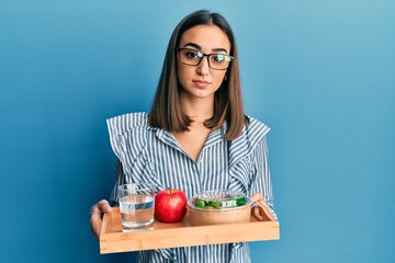 Young brunette girl holding tray with healthy lunch relaxed with serious expression on face. simple and natural looking at the camera.