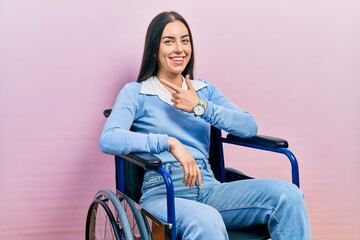 Beautiful woman with blue eyes sitting on wheelchair cheerful with a smile on face pointing with...
