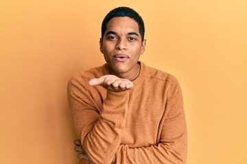 Young handsome hispanic man wearing casual winter sweater looking at the camera blowing a kiss with hand on air being lovely and sexy. love expression.