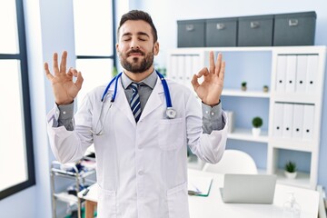 Handsome hispanic man wearing doctor uniform and stethoscope at medical clinic relax and smiling with eyes closed doing meditation gesture with fingers. yoga concept.