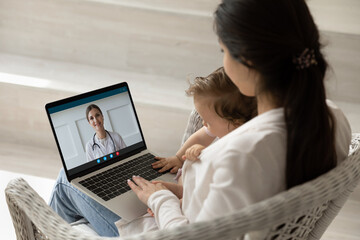 Loving mother hugging holding baby little daughter, using laptop, making video call to female...